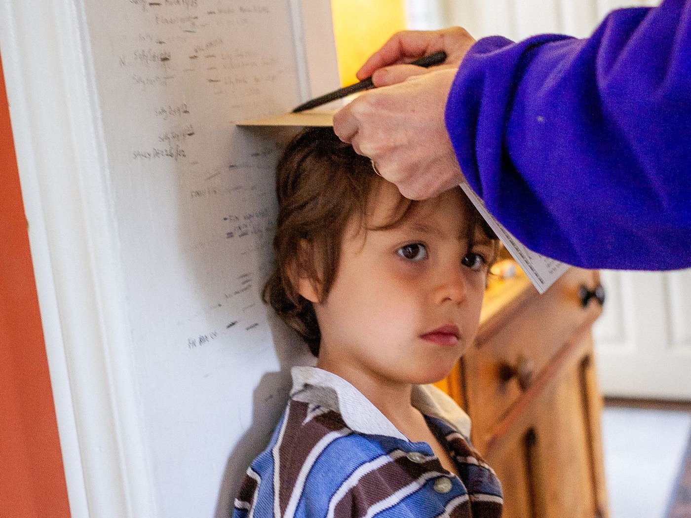 A child standing against a wall while a parent marks their height.